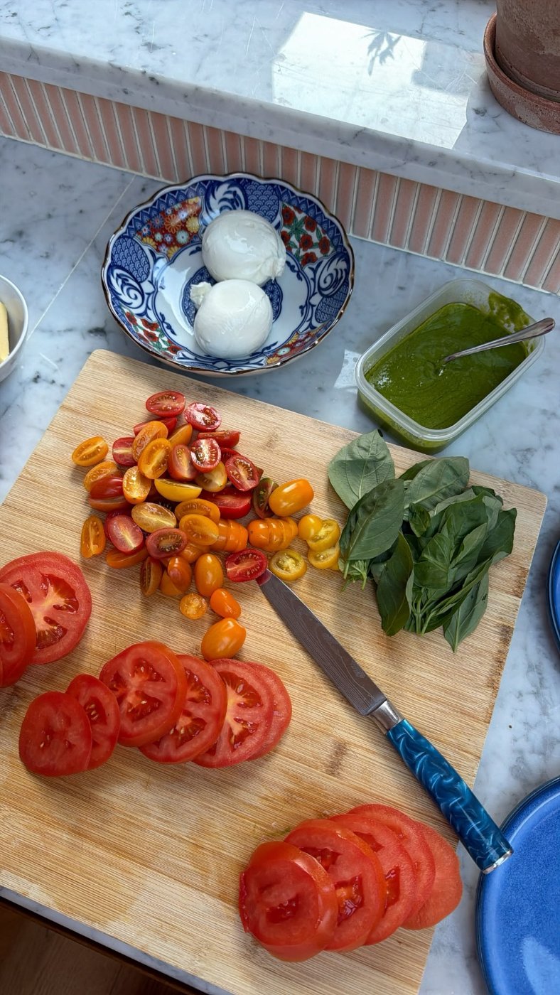 Burrata, sliced heirloom tomatoes, basil and pesto laid out on the marble counter