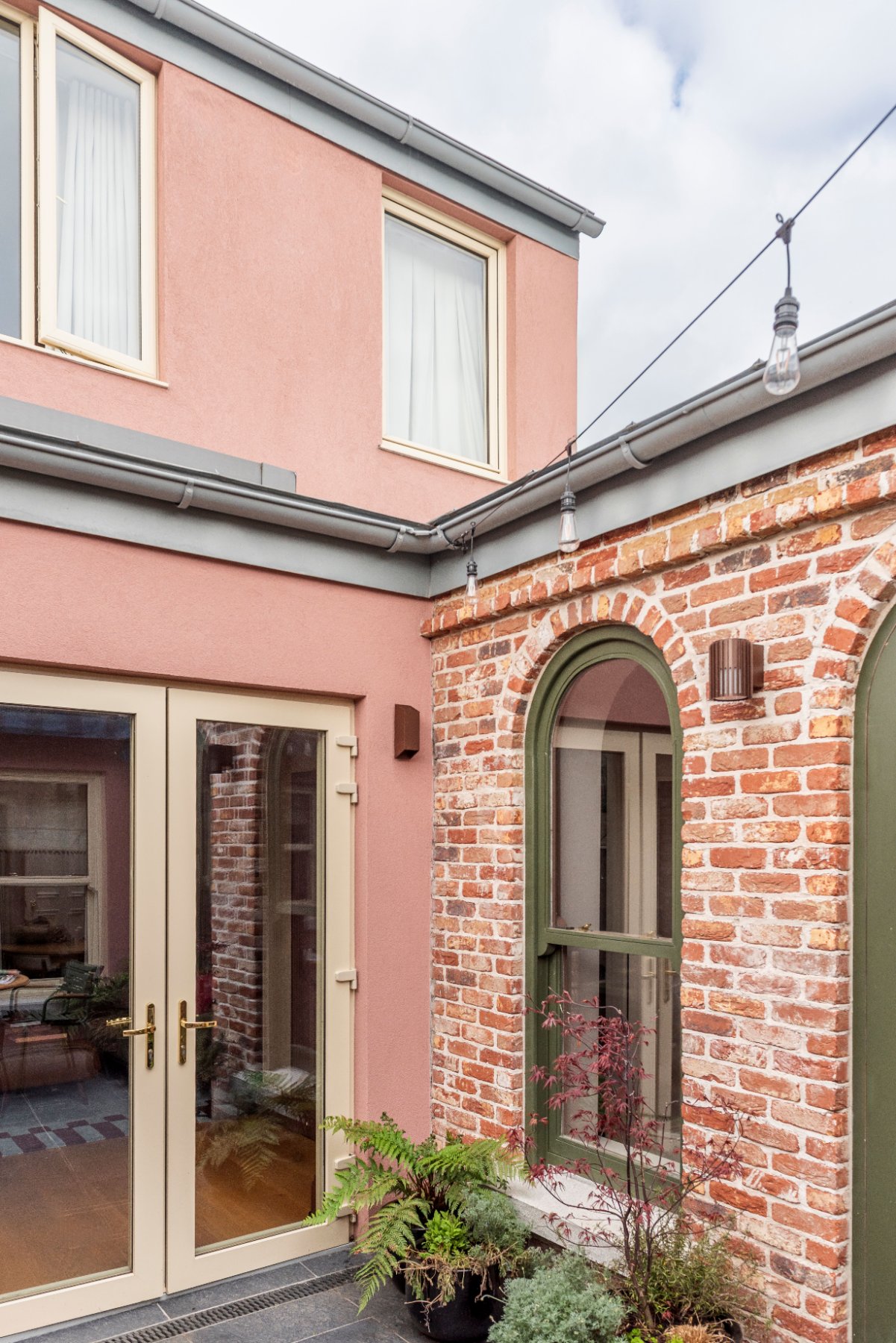 Pink render and red brick in the courtyard, with French doors, a green arched window and a Japanese maple