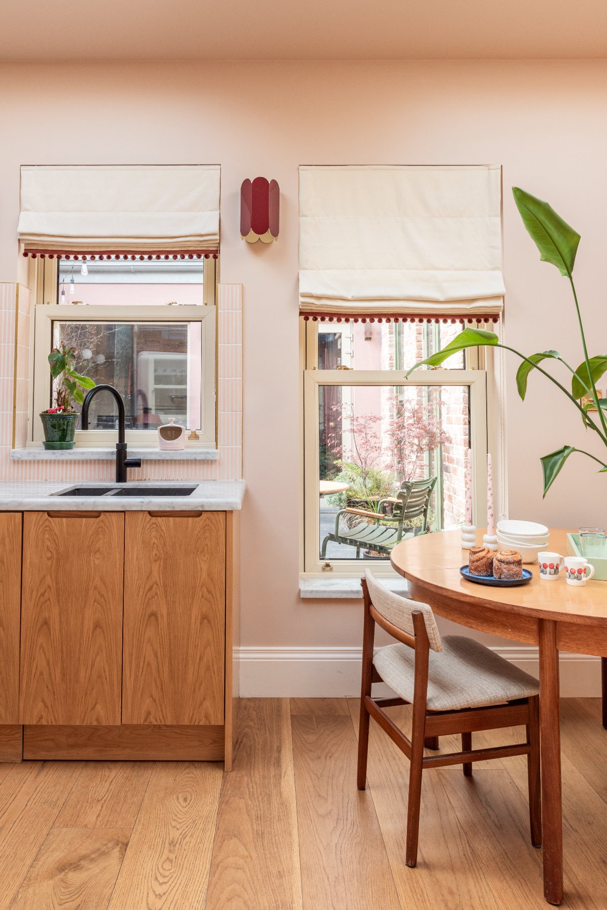 Pink kitchen with oak cabinets, two sash windows onto the courtyard and a round teak table set for coffee