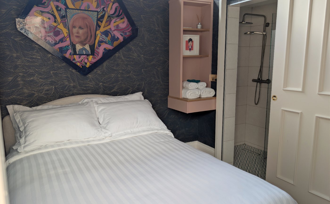 The small bedroom with Kiki Na Art's Moira Rose portrait above a king bed, and its ensuite shower