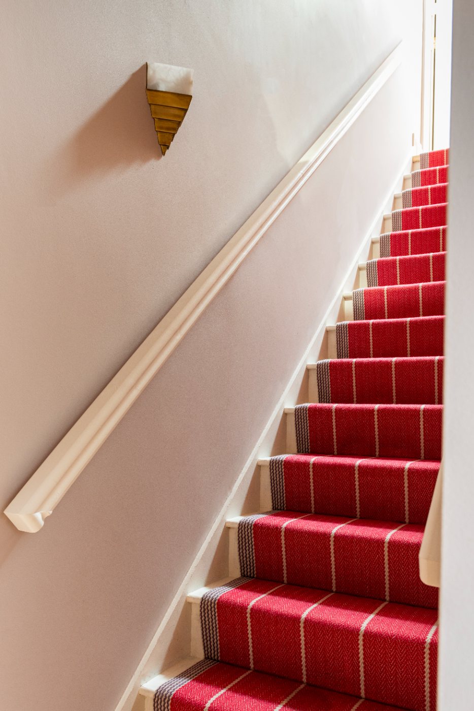 Stairs with a red striped runner and a brass wall light